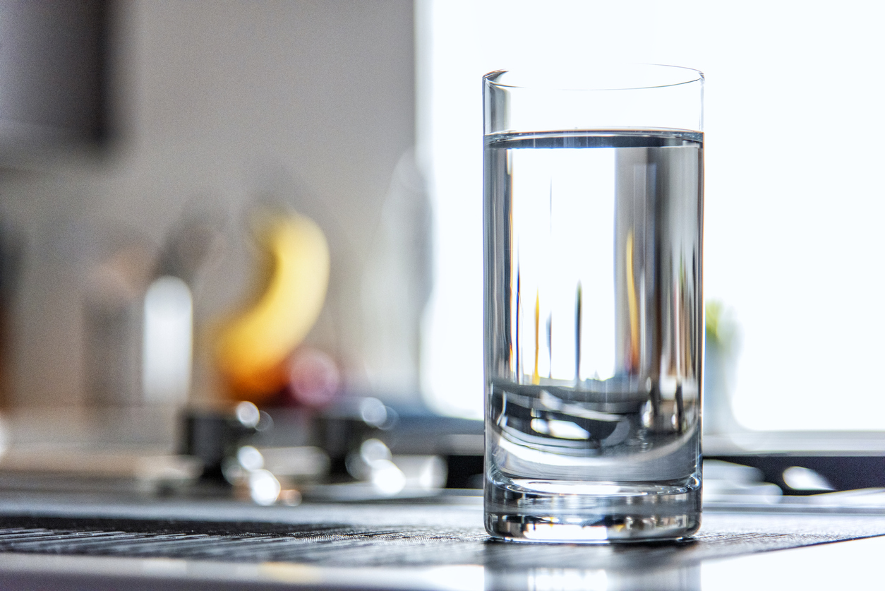 A glass filled with water atop a modern kitchen counter top inside a home.